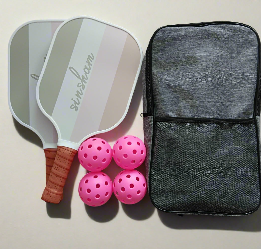 Two pickleball paddles with gray and brown colors, two pink indoor balls, two gray outdoor balls, and a black carrier bag.
