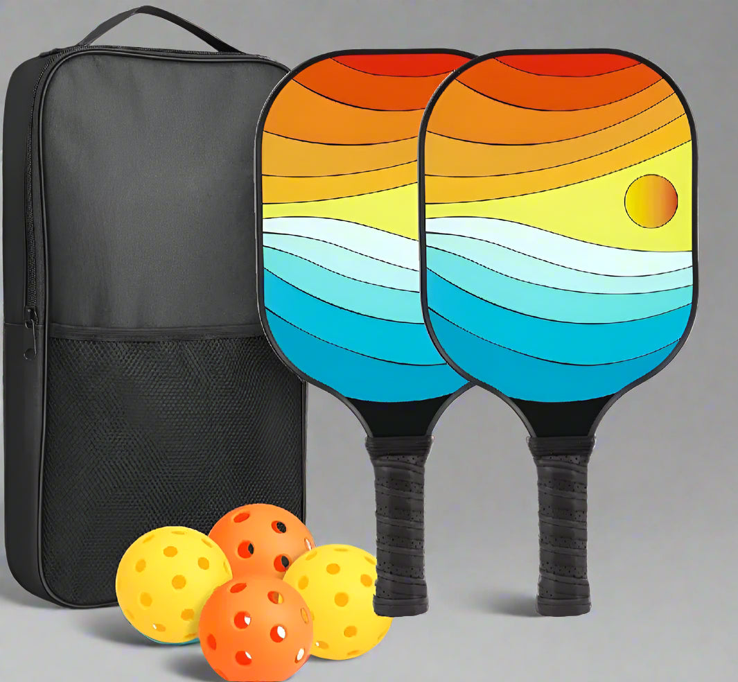 Sunset design Pickleball Paddle set of 2 with 2 paddles , 2 orange indoor balls, 2 yellow outdoor balls and a black bag. The paddle has a sunset design with a black handle and frame.