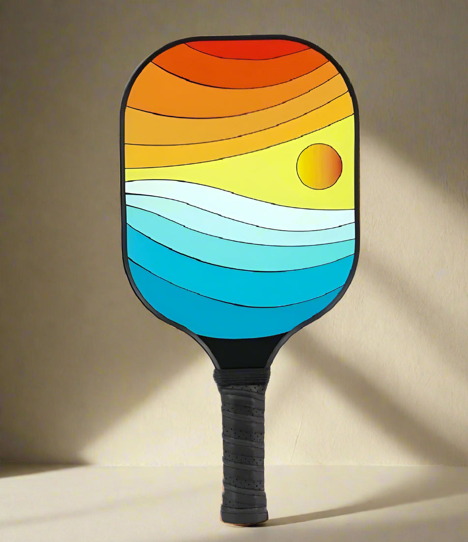 Sold as a single pickleball paddle with a artistic sunset design with the sea. Different shades of orange and blue making it very unique.