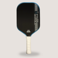 A pickleball paddle with a black face, blue trim, and a white grip, shown against a light gray background.