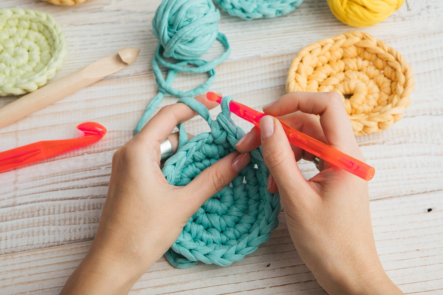 Close up photo of a women crocheting a circle with a orange crochet hook