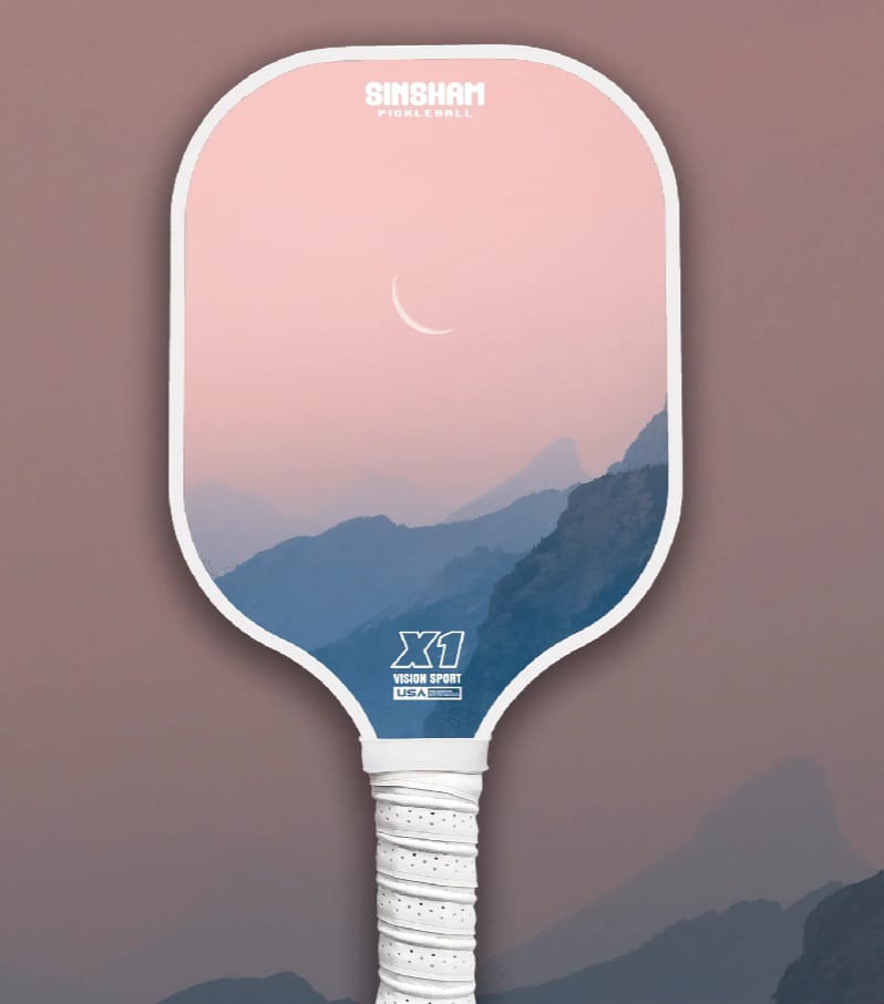 Single Pickleball Paddle with a design of a pink cotton candy-ish sky with a white crescent moon in the middle, with different shades of grey, faded mountains below in an artistic form. 
